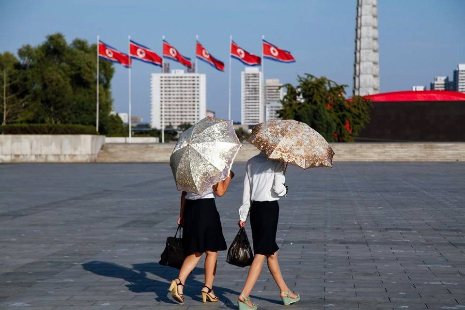 Two women with parasols cross a flag-lined plaza in Pyongyang, North Korea
