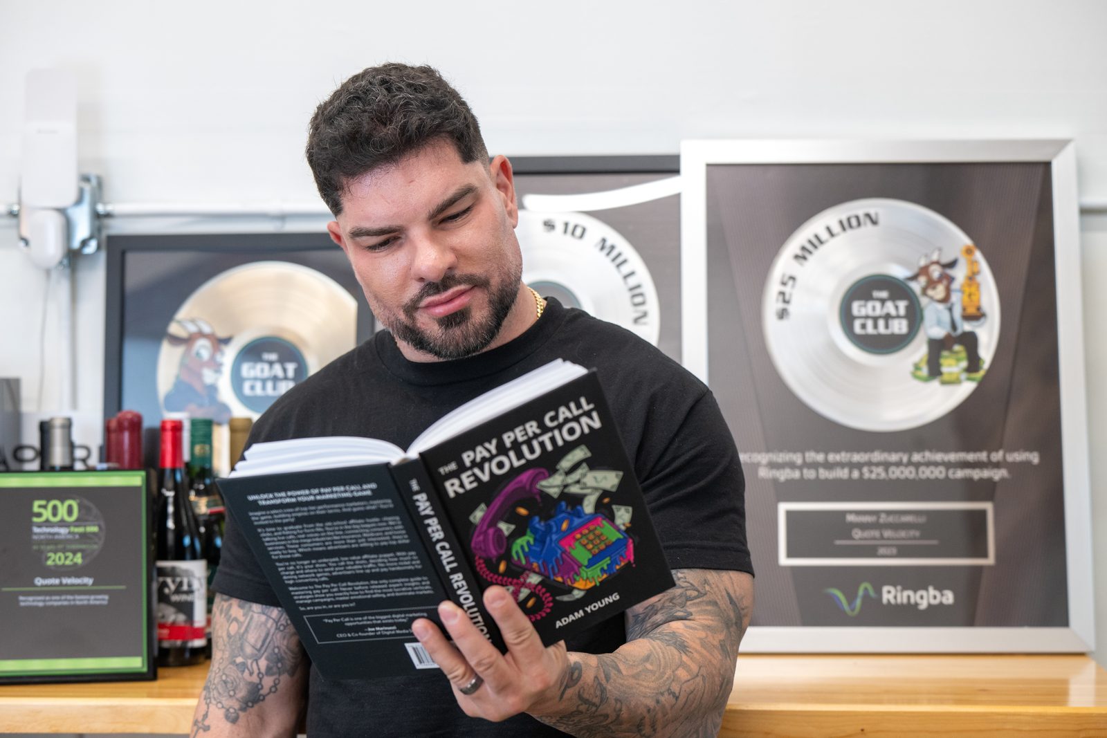 Manny Zuccarelli reading The Pay Per Call Revolution in front of his GOAT Club plaques