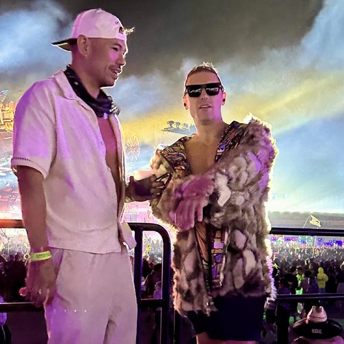 Adam Young in a fur coat and sunglasses with a friend at a festival at night