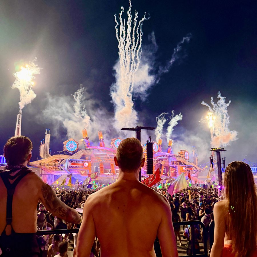 Adam Young and a friend with their arms up as fireworks burst over the festival crowd