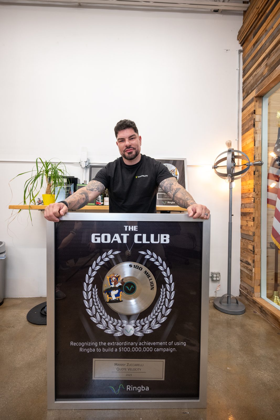 Manny Zuccarelli of QuoteVelocity leaning on his $100 million GOAT Club plaque