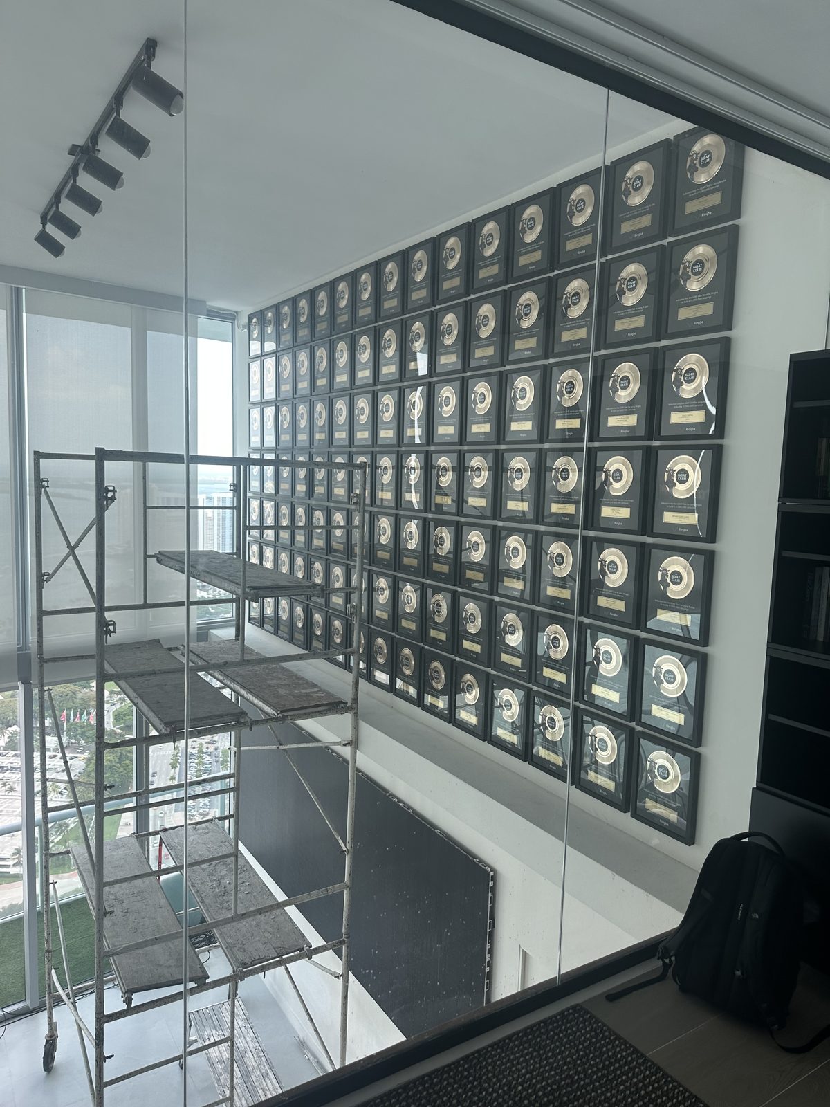 The GOAT Club plaque wall mid-installation, seen through the glass from upstairs with scaffolding below