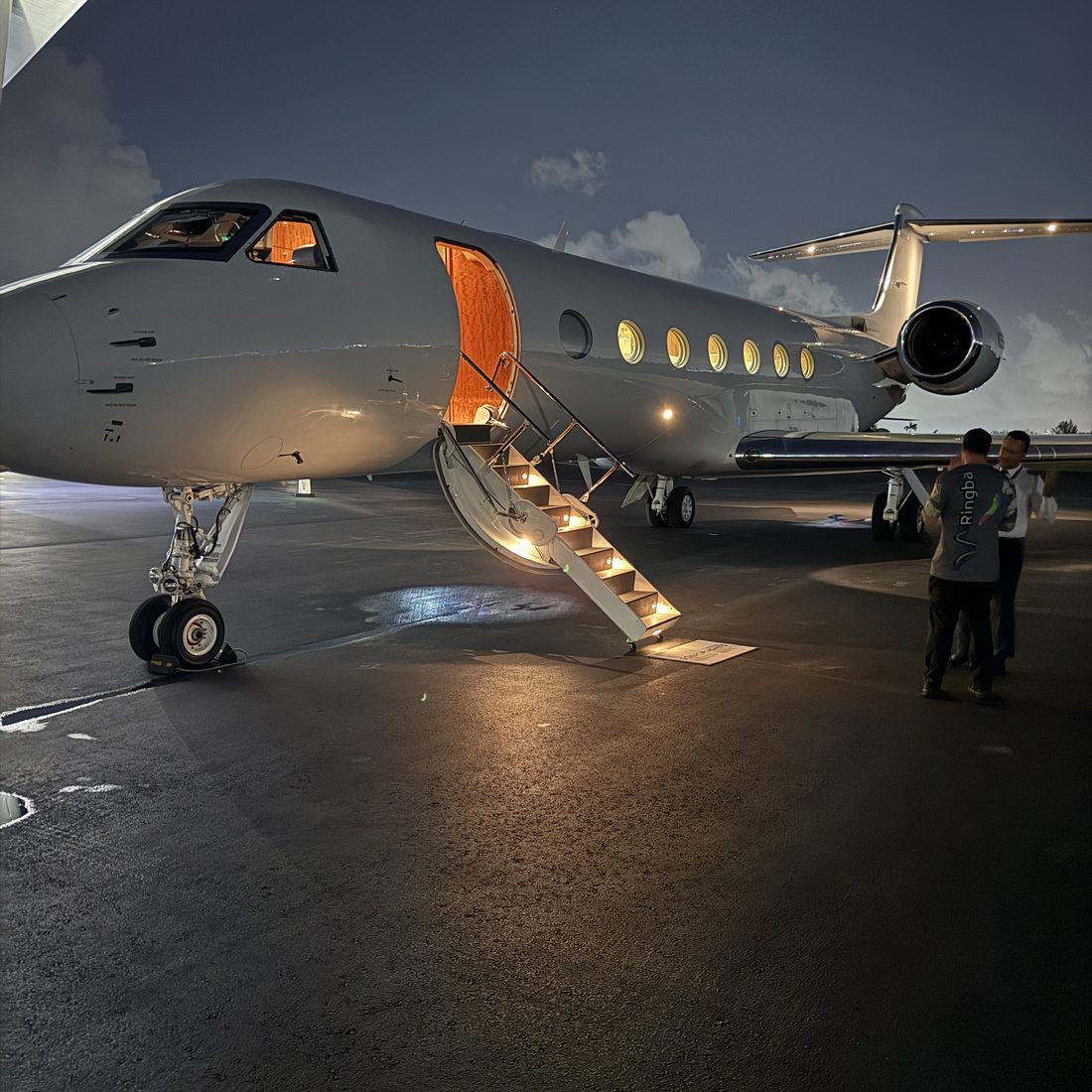 A Gulfstream G550 at dusk with its cabin lights on and airstair down