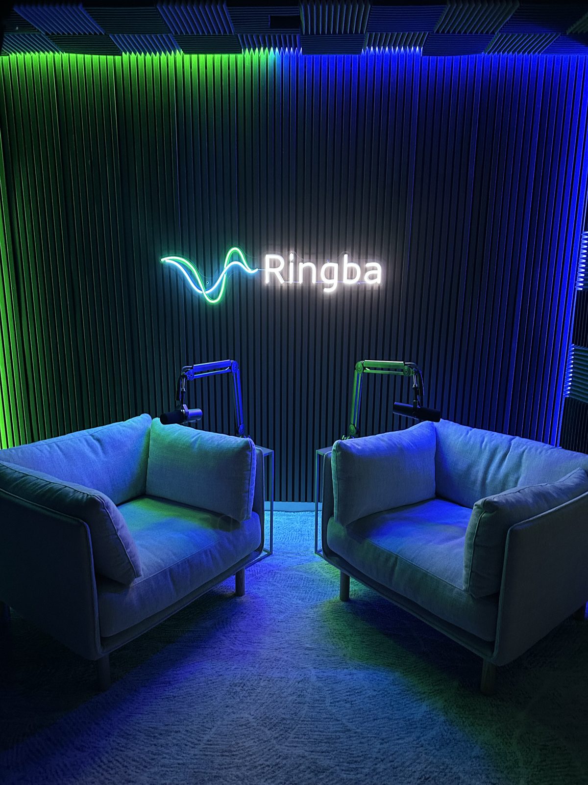 The Ringba podcast studio with two chairs and boom mics under a neon Ringba logo