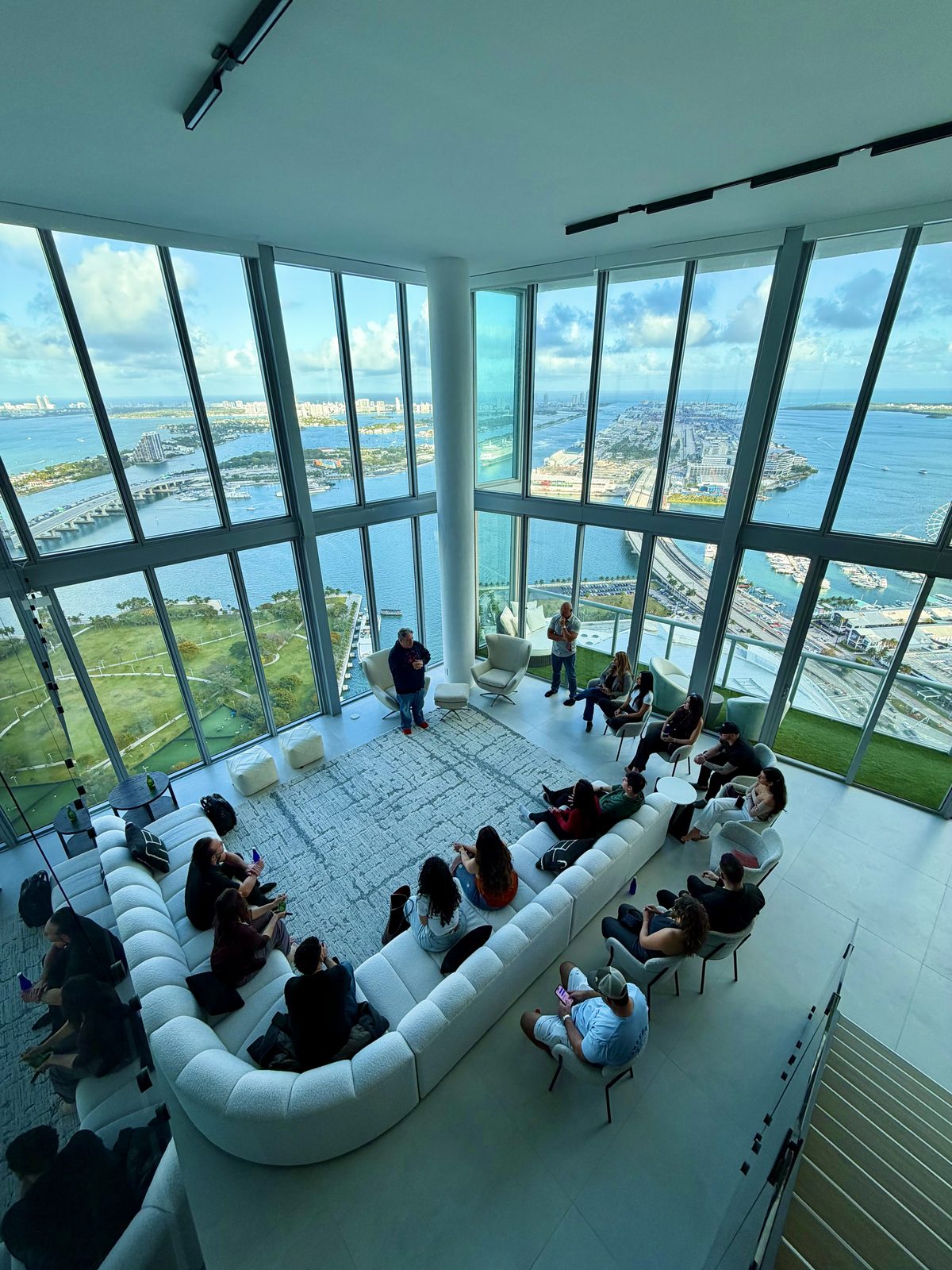 A mastermind session in the double-height penthouse great room, seats full around the curved sofa
