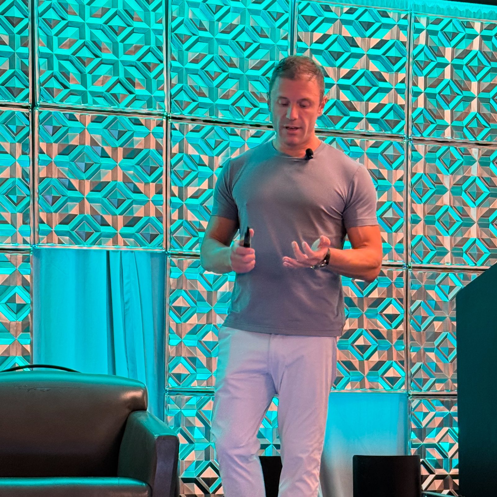 Adam Young speaking on a conference stage in front of a teal geometric backdrop